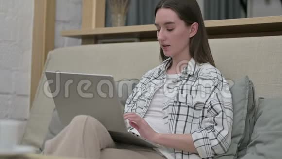 雄心勃勃的年轻女子在沙发笔记本电脑上庆祝成功视频的预览图