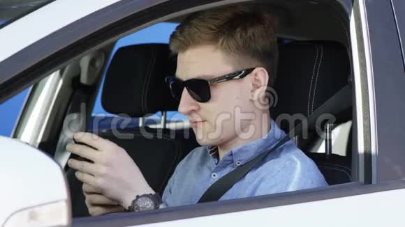 戴太阳镜的帅哥正在车里用手机聊天年轻人坐在车里打电话发短信视频的预览图