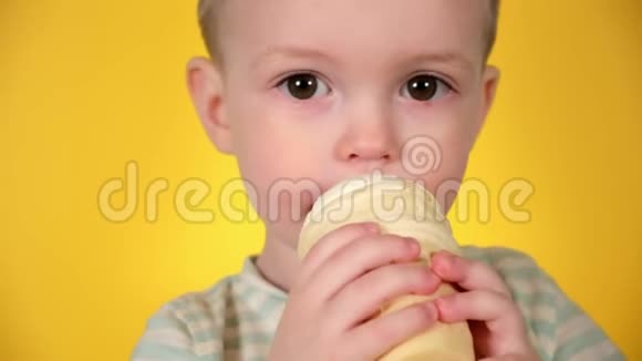可爱的金发男孩一边吃一边在华夫饼杯里享受冷冰淇淋在黄色的工作室背景下特写脸部画像视频的预览图