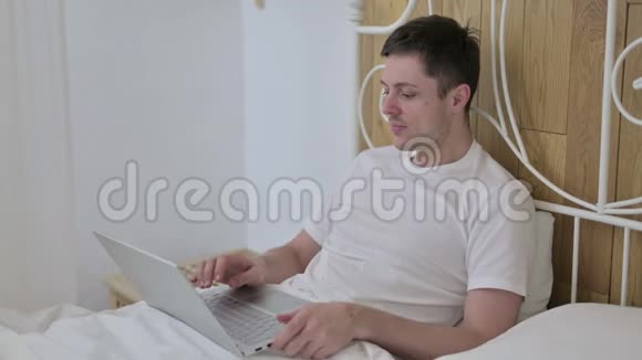 青年男子网上视频聊天在床上笔记本电脑视频的预览图