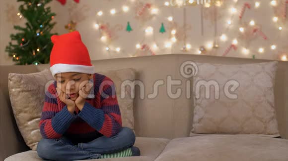 一个失望的小男孩独自坐在沙发上因为他没有收到他的圣诞礼物视频的预览图