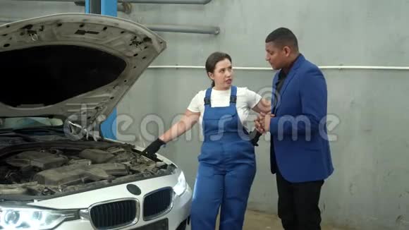 女技师在汽车修理厂给车主看一辆车视频的预览图