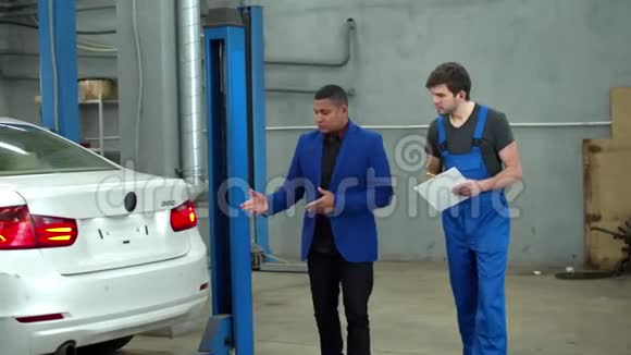 男子在汽车服务中向机械师展示汽车损坏情况视频的预览图