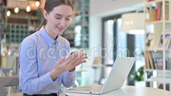 在咖啡厅使用带有笔记本电脑的智能手机的年轻女商人视频的预览图