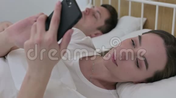 床上睡伴旁边使用智能手机的美女视频的预览图
