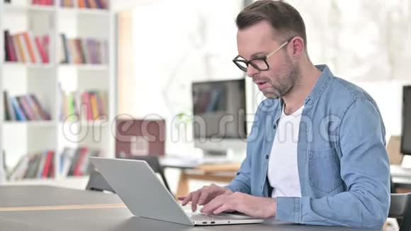 戴眼镜的年轻人在笔记本电脑上庆祝成功视频的预览图