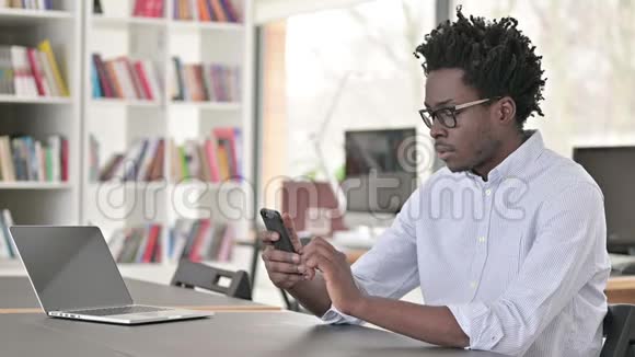 非洲男子在工作时在智能手机上浏览互联网视频的预览图