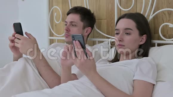 在床上使用智能手机的年轻夫妇视频的预览图