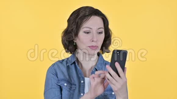 黄色背景下使用智能手机的老妇人视频的预览图