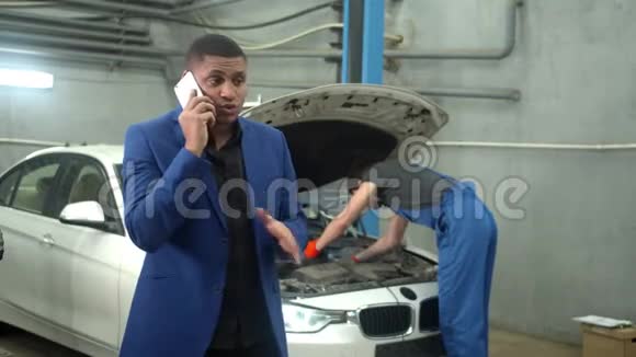 男人有感情地打电话机械师在后台修理一辆车视频的预览图