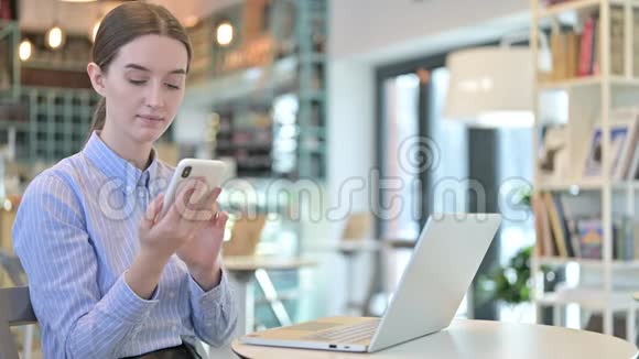 年轻女商人带着笔记本电脑使用智能手机视频的预览图