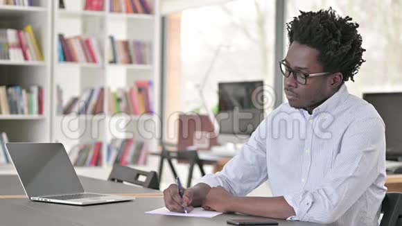 严肃的非洲男人在工作中写论文视频的预览图