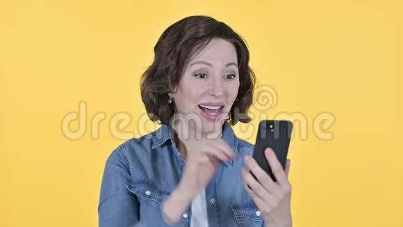老妇在智能手机上庆祝黄色背景视频的预览图