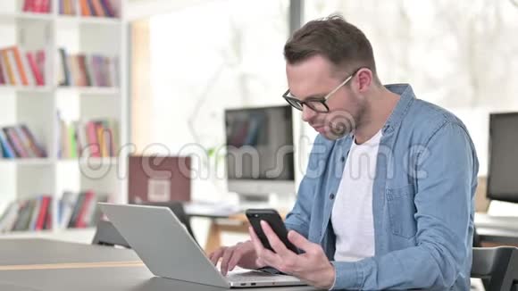 戴眼镜的年轻人用智能手机和笔记本电脑视频的预览图