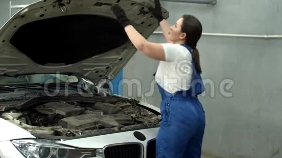 女机修工关闭汽车引擎盖在汽车服务中微笑视频的预览图