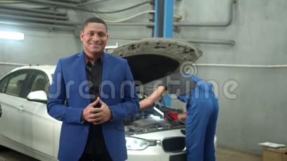穿西装的男人对着镜头微笑机械师在后台修理一辆车视频的预览图