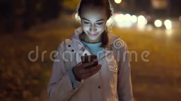 使用智能手机在夜间城市散步的漂亮微笑女人特写视频的预览图