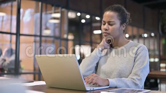 患有颈部疼痛的非洲妇女在笔记本电脑上工作视频的预览图