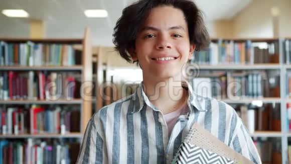 快乐少年带着书站在学校图书馆的慢镜头视频的预览图