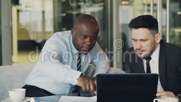两位商务同事正在看手提电脑并在玻璃墙的现代办公室讨论他们的项目视频的预览图