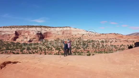 两名游客挥舞着手臂站在岩石的拱门上视频的预览图