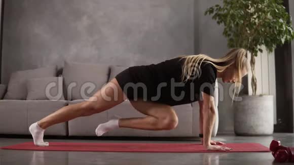 年轻的健康运动金发女孩与猪尾在黑色T恤黑色短做腿锻炼垫在明亮的房间做什么视频的预览图