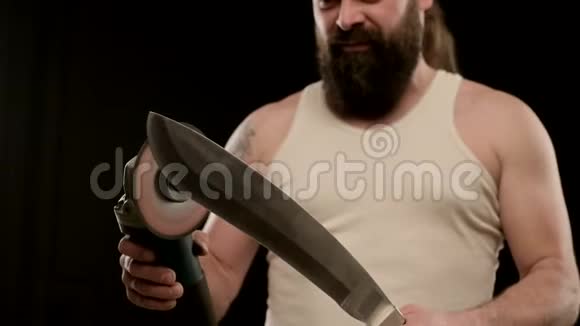一个留着胡须的男人穿着黑色工作室的T恤磨一把弯刀特写视频的预览图