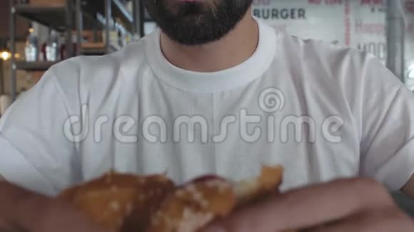 一个穿着白色t恤的男人的特写镜头咬了一个多汁的汉堡人吃汉堡4k4k录像慢动作30英尺视频的预览图