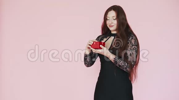美丽的红发女孩打开礼物羡慕欢喜3月8日的节日气氛粉色背景慢动作视频的预览图