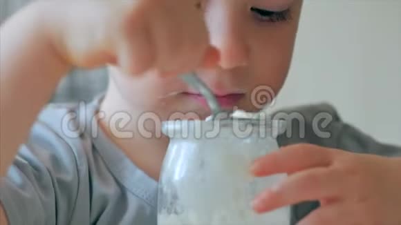 一个婴儿坐在桌子旁用勺子自己吃婴儿食品一个23岁的男孩急切地吃视频的预览图