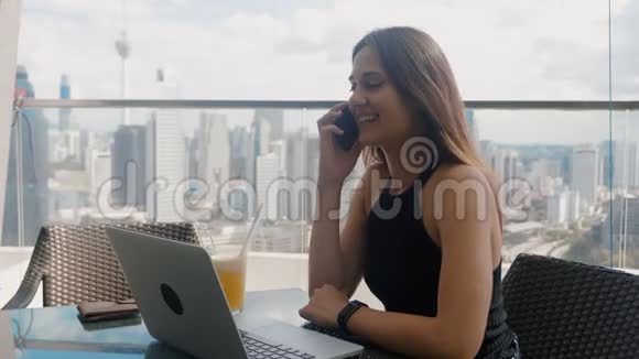 自信的商务女性正在一台笔记本电脑上工作她在商务中心的露台上打电话时尚视频的预览图