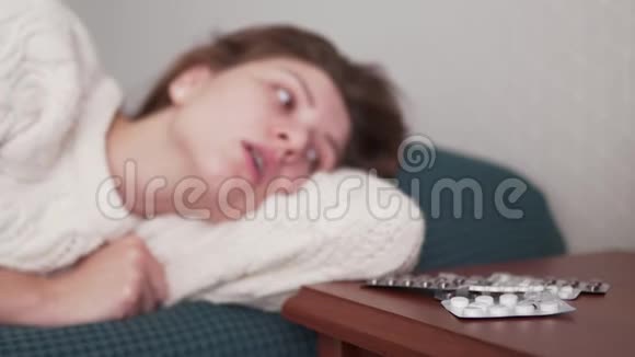 一个有感冒症状的生病的年轻女人躺在床上看着药物和药丸抗生素病毒治疗视频的预览图