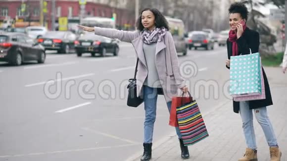 两个有魅力的非洲裔美国妇女带着购物袋从商场销售回来时叫出租车视频的预览图