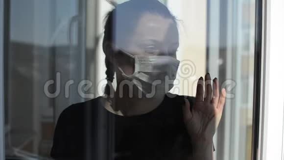 戴着医用口罩的年轻女孩站在窗口视频的预览图
