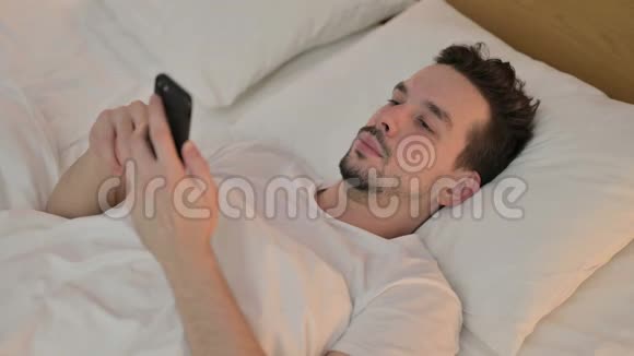 年轻人在床上使用智能手机视频的预览图