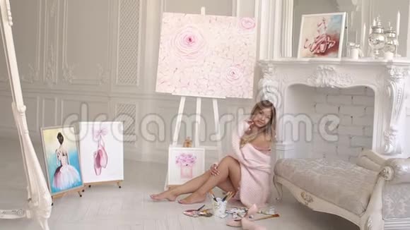 女孩艺术家坐在工作室的地板上她的许多画视频的预览图