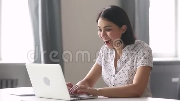 喜出望外的亚洲商界女赢家看着笔记本电脑视频的预览图