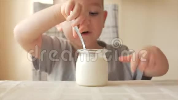 小男孩坐在桌子旁独自用勺子吃婴儿食品一个23岁的男孩急切地吃牛奶视频的预览图