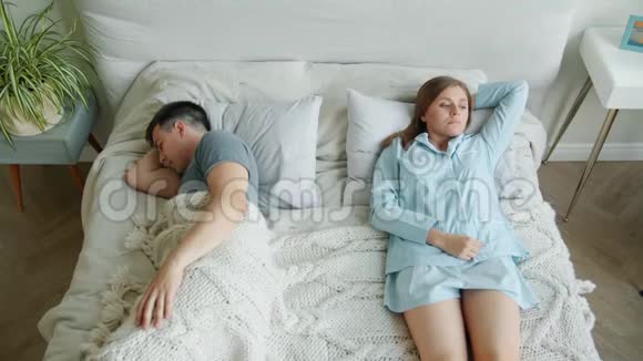 穿着睡衣的悲伤女孩躺在床上叹息而男朋友睡在家里视频的预览图