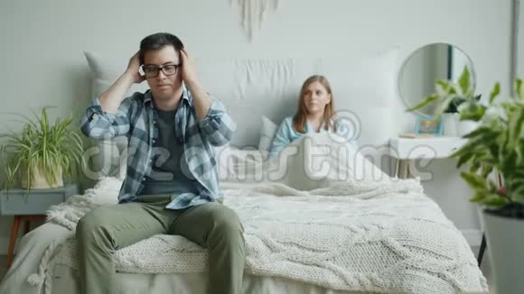 不开心的男人坐在床上抚摸着伤心的脸而生气的妻子在家里大喊大叫视频的预览图