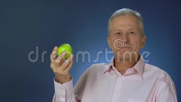 一个身材苗条的中年男人穿着粉红色的衬衫正高兴地吃着一个绿色多汁的苹果视频的预览图