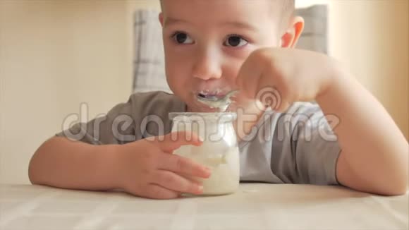 一个婴儿坐在桌子旁用勺子自己吃婴儿食品一个23岁的男孩急切地吃视频的预览图