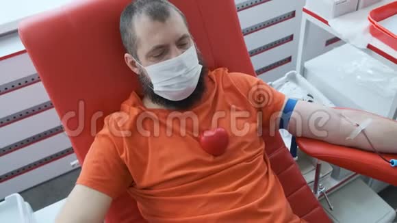 一个留着胡子的捐献者躺在沙发上胸前有一颗红色的橡胶心人捐献静脉血献血视频的预览图