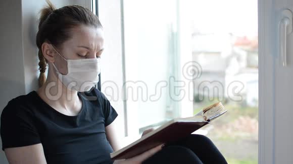 一个戴着医用口罩的年轻女孩坐在靠近窗户的窗台上看书视频的预览图