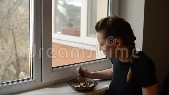 靠近窗户的年轻女子吃巧克力早餐麦片和酸奶视频的预览图