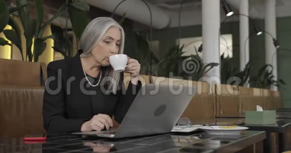一边观看老优雅的女商人喝咖啡和工作笔记本电脑成熟美丽的雌性小肠神经元视频的预览图