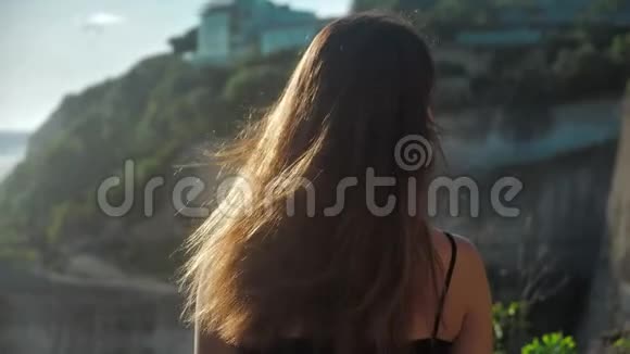 特写一个女孩的肖像她站在悬崖上看着大海她的头发是吹风的日落背景视频的预览图