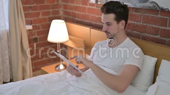 在床上的平板电脑上视频聊天的年轻人视频的预览图