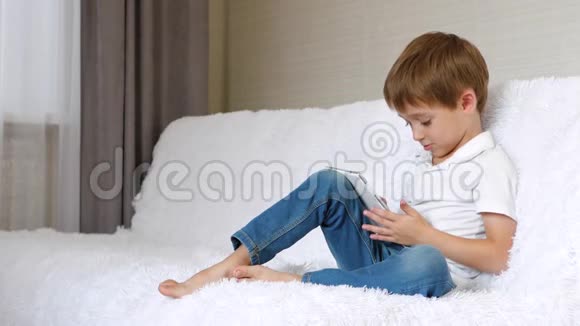 一个快乐的孩子坐在沙发上放松玩用平板电脑读电子书视频的预览图