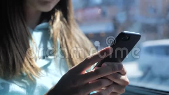 一个年轻的女人正在公共汽车上点击智能手机在窗外阳光明媚的一天背景上的棕榈树4k视频的预览图